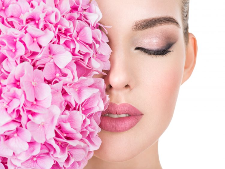 Young beautiful woman with flowers near face. Beauty treatment concept. Skin care. Pretty female with health, fresh skin of body. Lady with pink makeup of eyes.